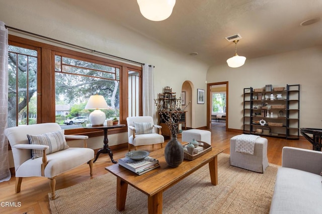 living area featuring arched walkways, visible vents, a healthy amount of sunlight, and wood finished floors