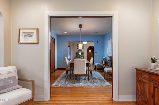 dining room with light wood-style floors, arched walkways, and baseboards