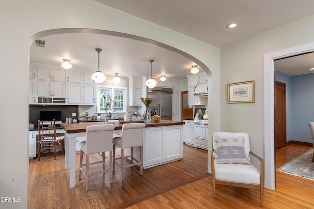 kitchen with white cabinets, white gas range oven, built in refrigerator, wood counters, and light wood-type flooring