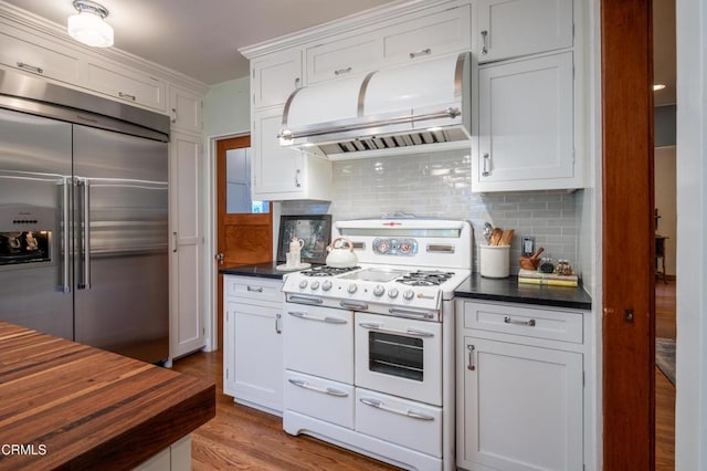 kitchen featuring stainless steel built in refrigerator, under cabinet range hood, double oven range, tasteful backsplash, and white cabinets