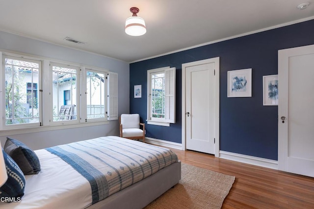 bedroom with visible vents, baseboards, wood finished floors, and crown molding