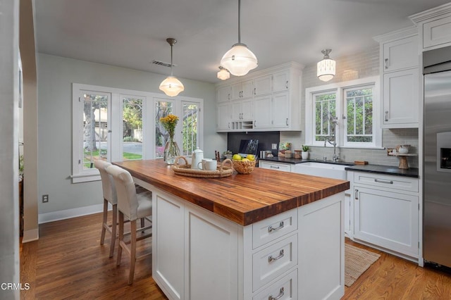 kitchen with butcher block countertops, stainless steel built in fridge, wood finished floors, white cabinets, and a sink