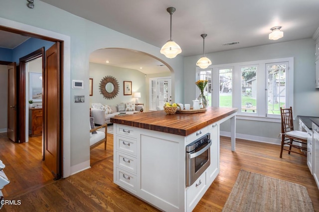 kitchen with visible vents, open floor plan, butcher block counters, dark wood-style floors, and arched walkways