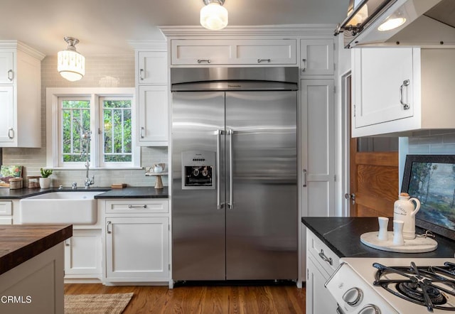 kitchen with stainless steel built in fridge, under cabinet range hood, a sink, tasteful backsplash, and white cabinets