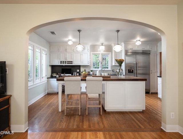 kitchen with dark wood finished floors, white cabinets, arched walkways, and stainless steel built in refrigerator