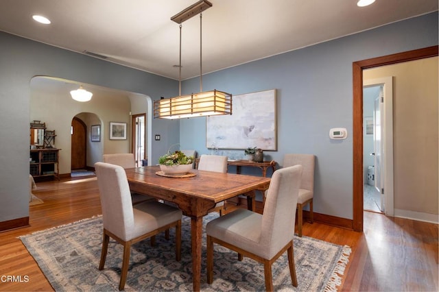 dining area with arched walkways, recessed lighting, light wood-type flooring, and baseboards