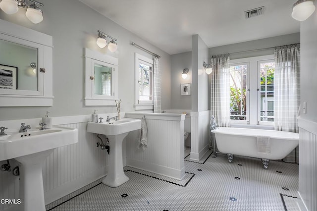 bathroom featuring a wealth of natural light, visible vents, a soaking tub, and wainscoting