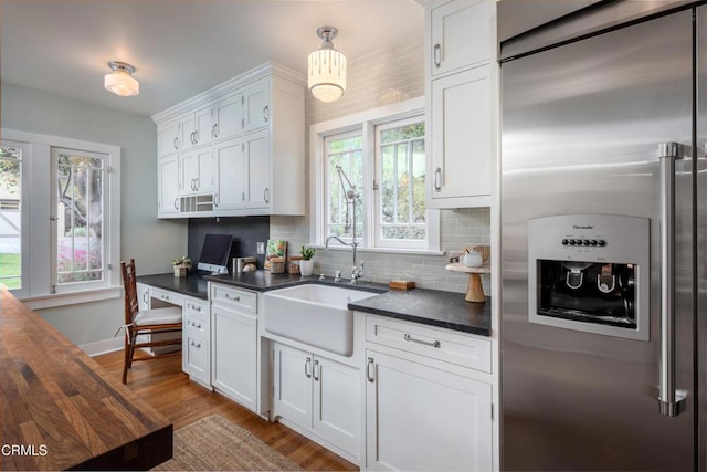 kitchen featuring a sink, dark countertops, white cabinetry, decorative backsplash, and high end refrigerator