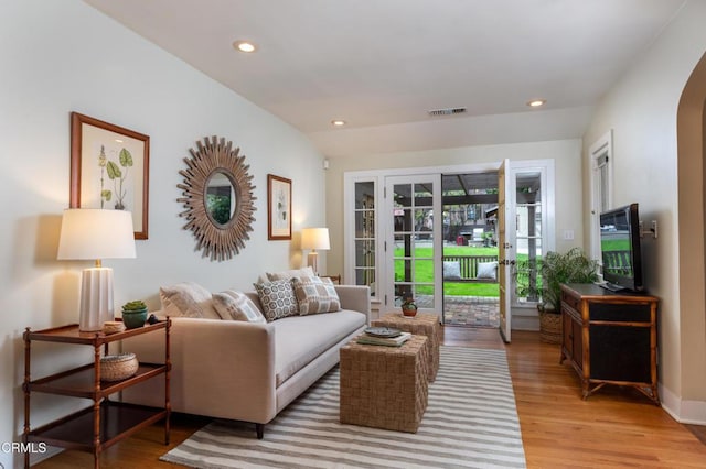 living area with arched walkways, recessed lighting, light wood-type flooring, and vaulted ceiling