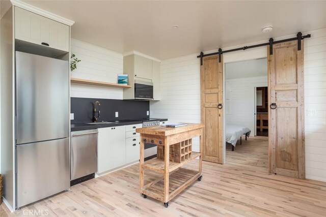 236 Avenida Montalvo, San Clemente, CA 92672 - kitchen featuring appliances with stainless steel finishes, a barn door, light wood-type flooring, dark countertops, and wood walls