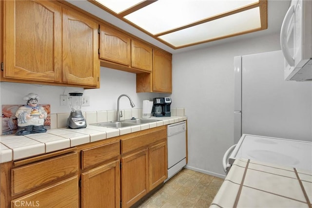 kitchen with white appliances, brown cabinetry, light floors, baseboards, and a sink