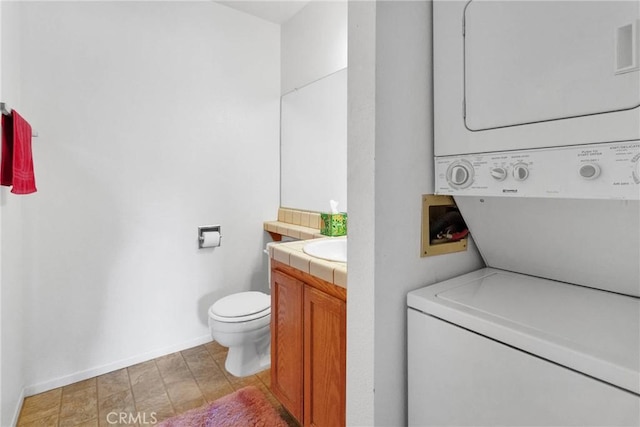 bathroom featuring toilet, stacked washing maching and dryer, vanity, and baseboards