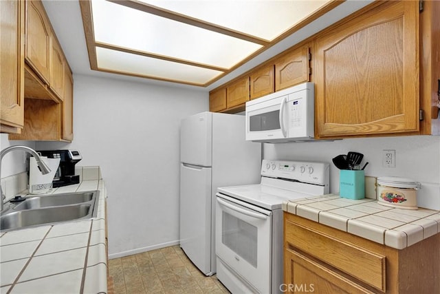 kitchen featuring brown cabinets, a sink, white appliances, baseboards, and tile counters