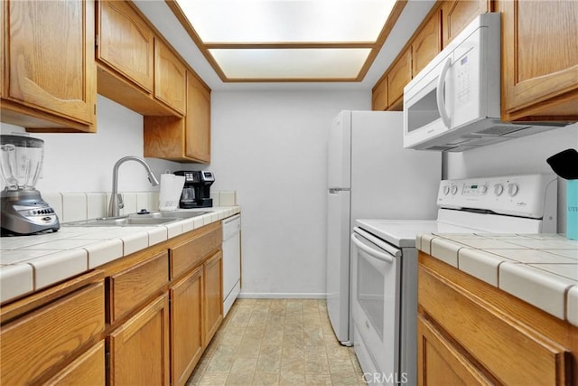 kitchen with brown cabinets, a sink, white appliances, baseboards, and tile counters