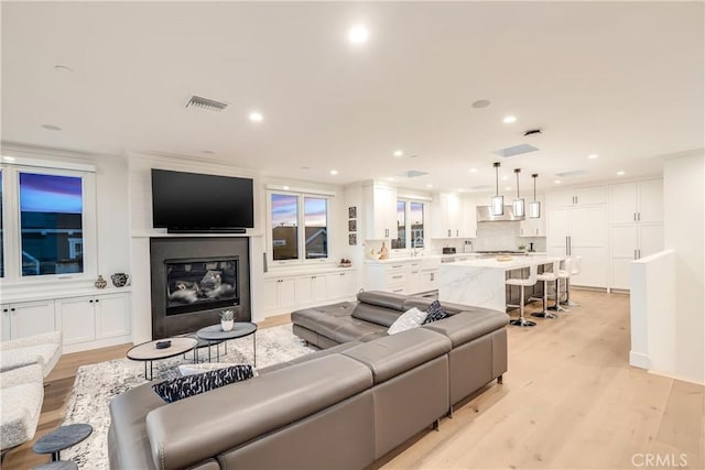 living room with recessed lighting, visible vents, a glass covered fireplace, and light wood-style flooring