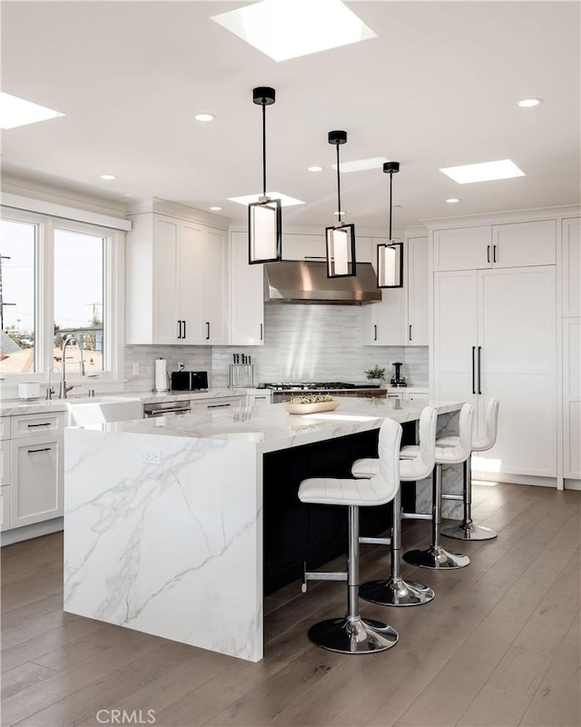 kitchen featuring tasteful backsplash, a center island, under cabinet range hood, a skylight, and white cabinetry