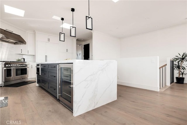 kitchen with beverage cooler, double oven range, light wood-style floors, under cabinet range hood, and white cabinetry