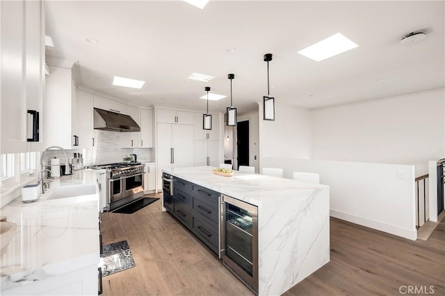 kitchen with beverage cooler, under cabinet range hood, a sink, stainless steel appliances, and white cabinets