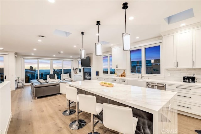 kitchen featuring stainless steel dishwasher, light wood finished floors, white cabinetry, and a center island