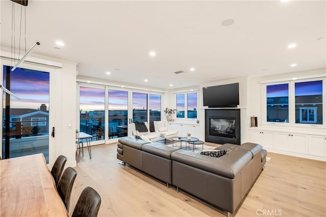 living room featuring recessed lighting, light wood-style flooring, and a glass covered fireplace