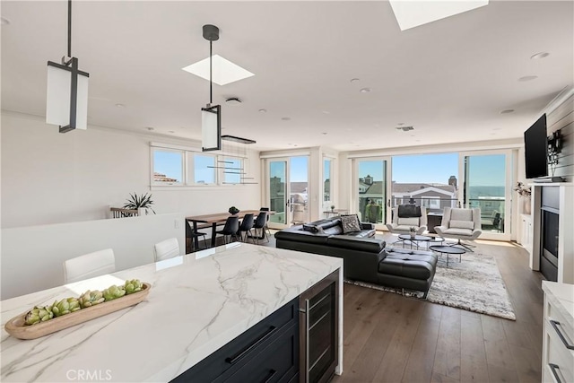 kitchen with dark wood-type flooring, beverage cooler, dark cabinetry, a skylight, and light stone countertops