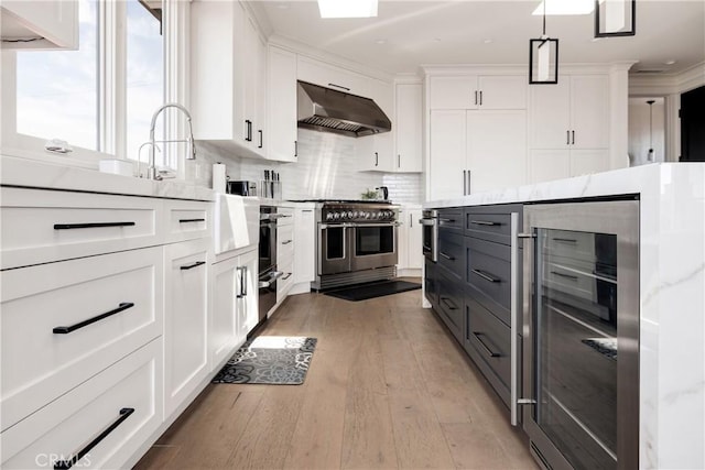 kitchen with under cabinet range hood, beverage cooler, double oven range, light wood-style floors, and white cabinetry