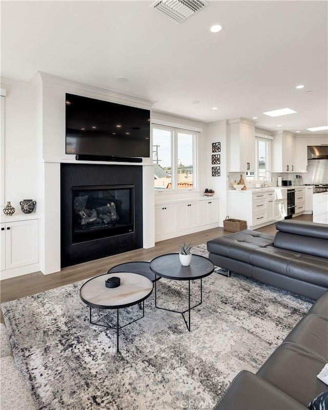 living area with recessed lighting, visible vents, wood finished floors, and a glass covered fireplace