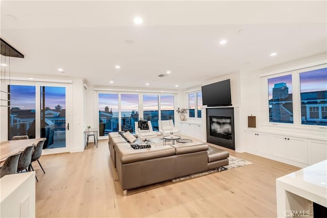 living room featuring recessed lighting, a glass covered fireplace, and light wood finished floors