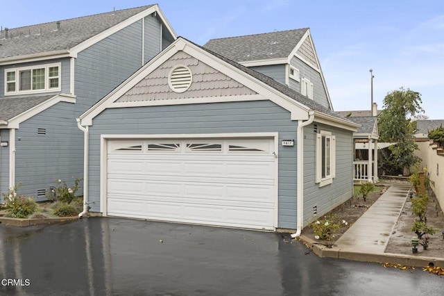 exterior space featuring driveway, a shingled roof, a garage, and fence