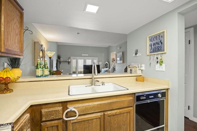 kitchen featuring a sink, a peninsula, brown cabinetry, and light countertops