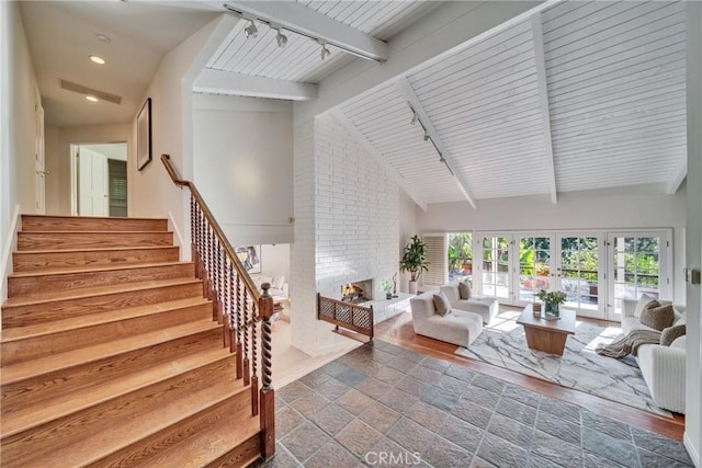 interior space with beamed ceiling, high vaulted ceiling, rail lighting, a brick fireplace, and stairs