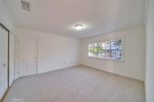 unfurnished bedroom featuring baseboards, visible vents, ornamental molding, a closet, and light colored carpet