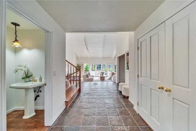 hallway featuring stairs, beam ceiling, baseboards, and stone finish flooring