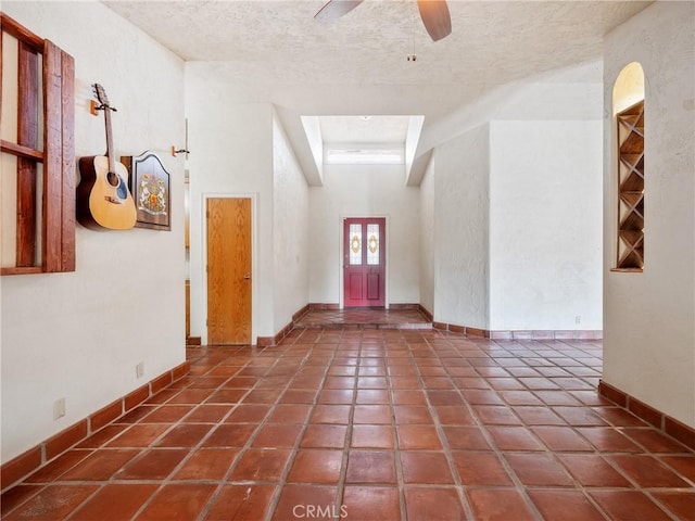 entrance foyer featuring a ceiling fan, a textured ceiling, a high ceiling, tile patterned flooring, and baseboards