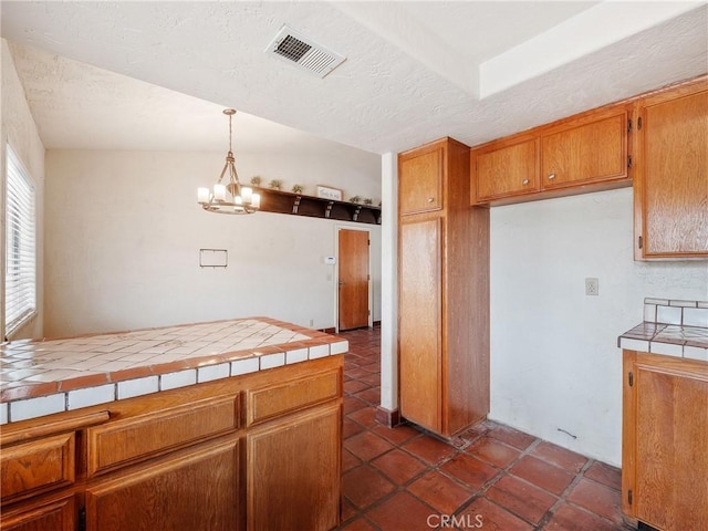 kitchen featuring tile counters, brown cabinetry, visible vents, and a chandelier