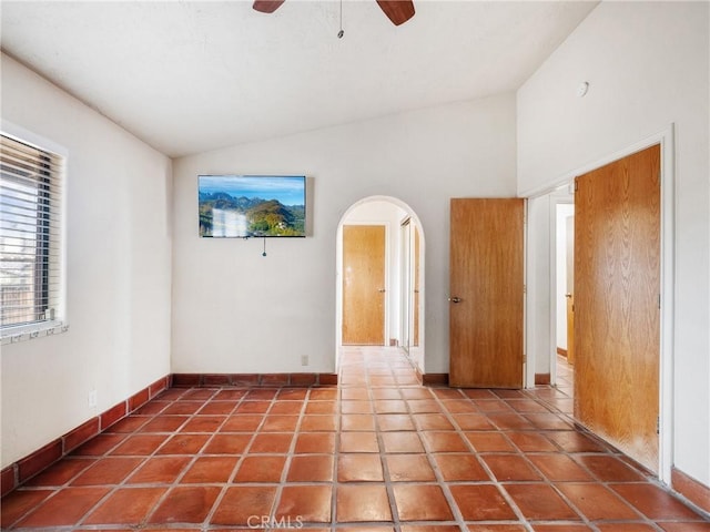 tiled spare room with arched walkways, baseboards, ceiling fan, and vaulted ceiling