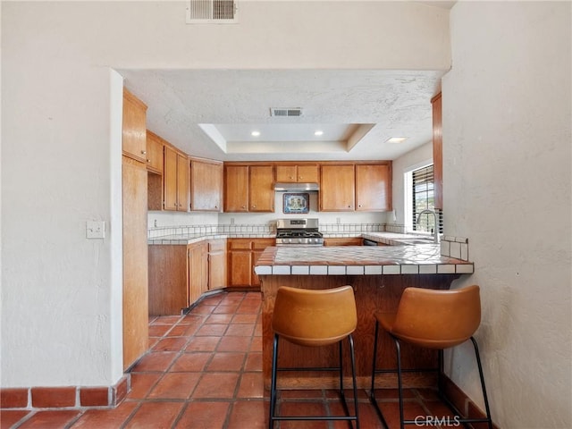 kitchen with visible vents, a raised ceiling, a peninsula, gas range, and tile counters