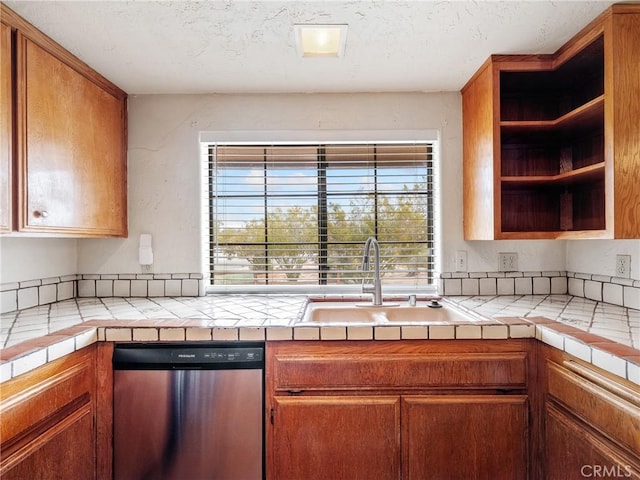 kitchen with brown cabinets, a sink, open shelves, stainless steel dishwasher, and a textured ceiling