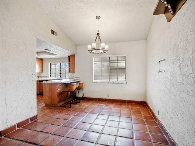 kitchen featuring vaulted ceiling, a textured wall, visible vents, and brown cabinets