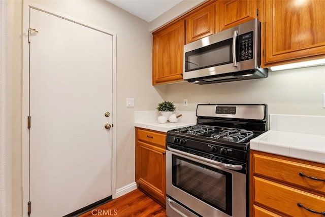 kitchen with dark wood finished floors, brown cabinets, stainless steel appliances, and tile counters