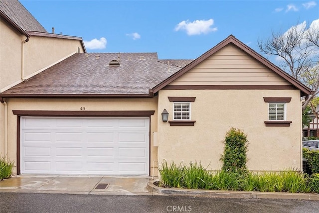 exterior space with a garage, stucco siding, and roof with shingles