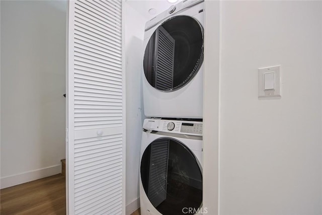 clothes washing area featuring stacked washer / drying machine, baseboards, wood finished floors, and laundry area