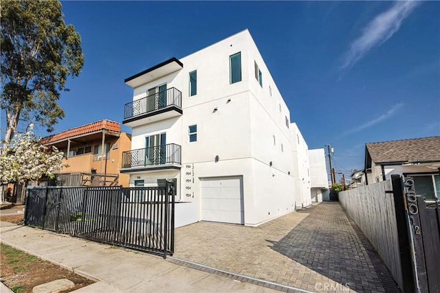 view of front of home featuring a balcony, stucco siding, a garage, and fence