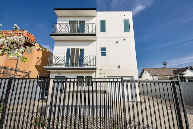 view of front of house featuring stucco siding, a balcony, and a fenced front yard