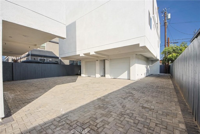 view of home's exterior featuring decorative driveway, fence, a garage, and stucco siding