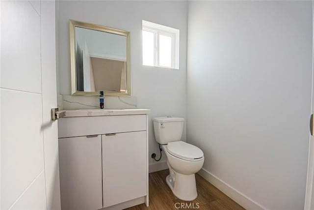 half bathroom with baseboards, toilet, wood finished floors, and vanity