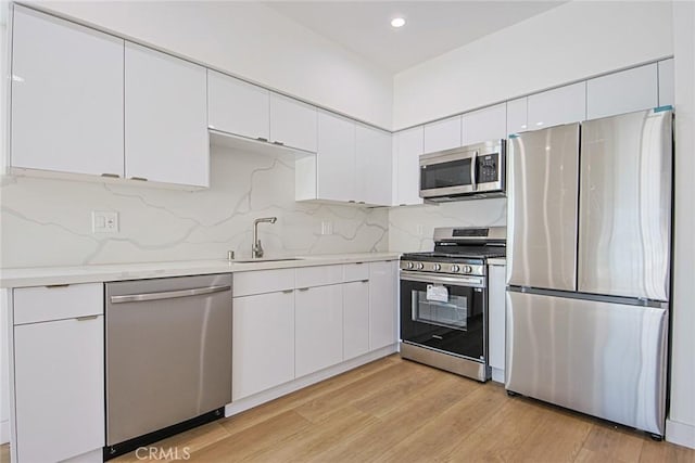 kitchen featuring light wood-type flooring, light countertops, appliances with stainless steel finishes, white cabinets, and a sink