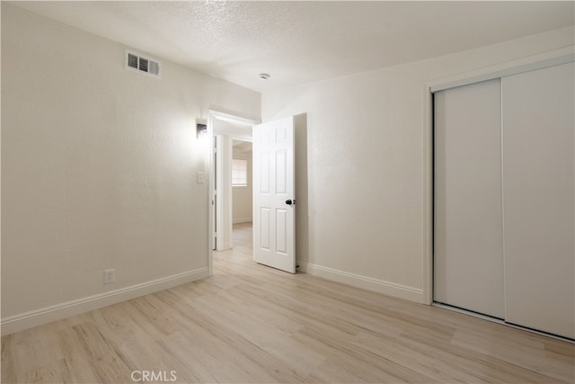 unfurnished bedroom with visible vents, baseboards, light wood-style floors, and a closet