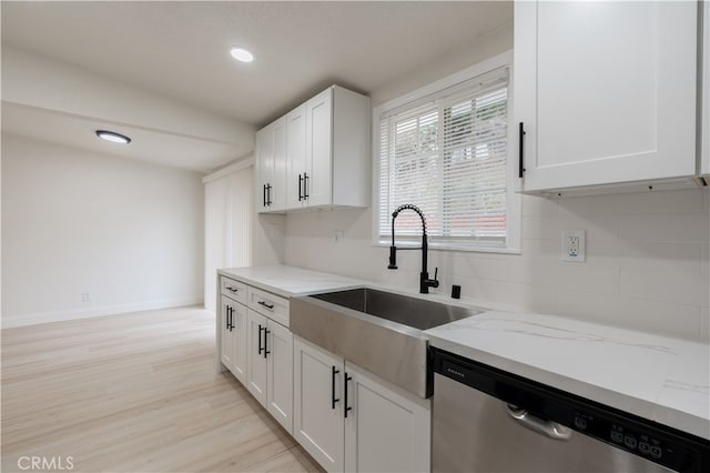 kitchen featuring stainless steel dishwasher, light stone counters, white cabinetry, and a sink