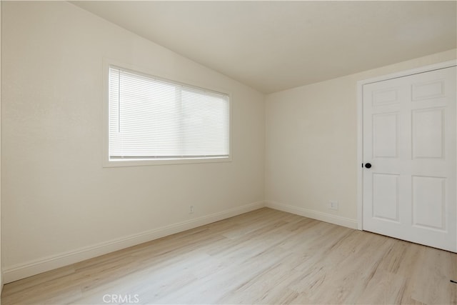 empty room featuring lofted ceiling, wood finished floors, and baseboards